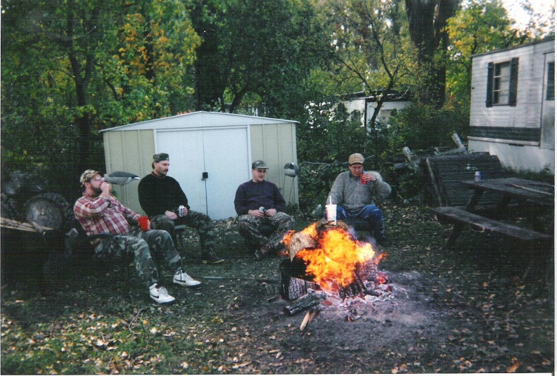 L. to R.: Dwight “D” Stever, Mel Oliva, John “E” Ellis, and Mitch “Spence” Baier sitting around a bonfire at the Riverside Acres cabin.